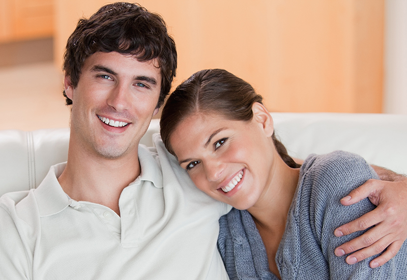 Man with his left arm around his wife's shoulder while sitting on their couch